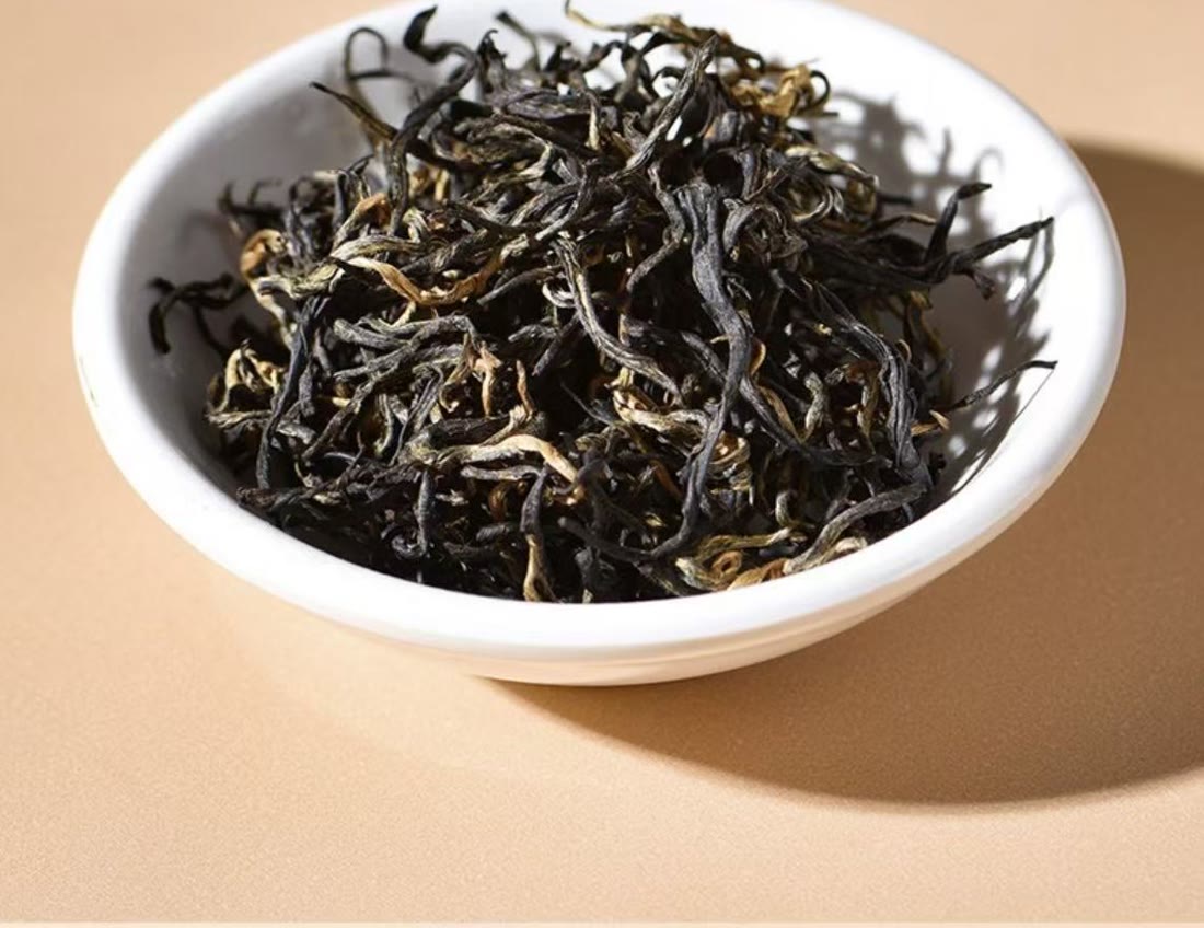 Dry Honey Black Tea leaves in a white bowl, thin dark twists with golden tips